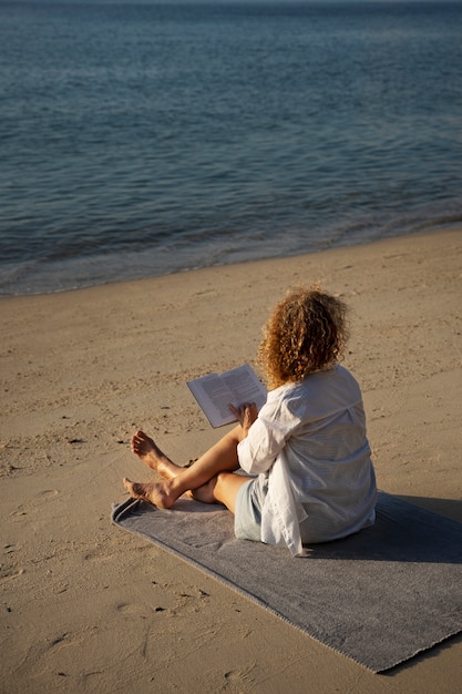 Kostenloses Foto volle schussfrau, die auf strand liest