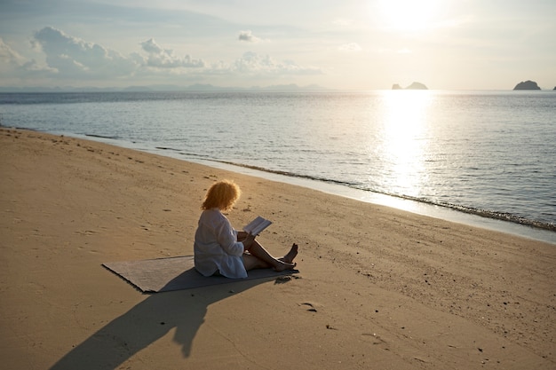 Volle Schussfrau, die auf Strand liest