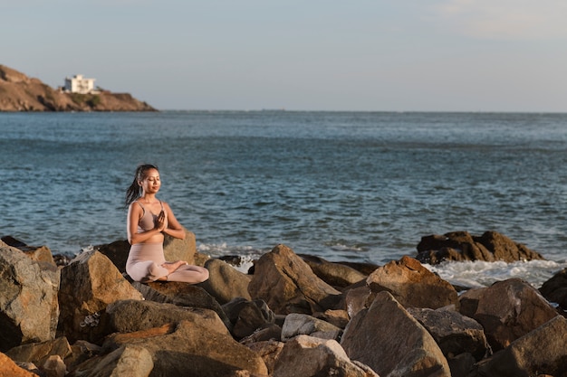 Volle Schussfrau, die Yoga auf Felsen tut