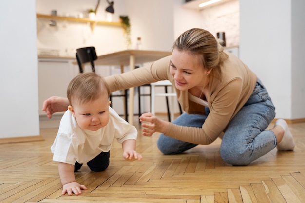 Volle Schussmutter, die das Krabbeln des Babys beobachtet