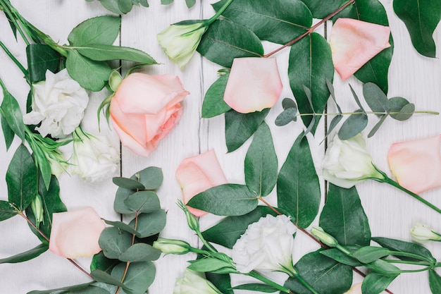 Voller Rahmen von Blättern; Eustoma und Rosarosenblumen auf hölzernem Schreibtisch