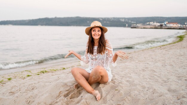 Voller Schuss glückliche Frau, die auf Sand sitzt