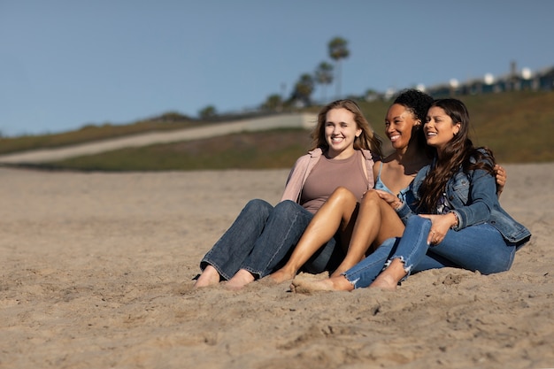 Kostenloses Foto voller schuss glückliche frauen, die zusammen am strand sitzen