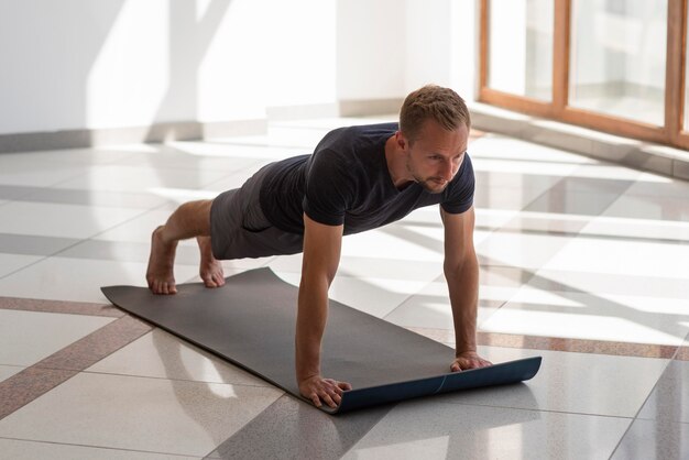 Voller Schuss junger Mann, der Yoga drinnen praktiziert