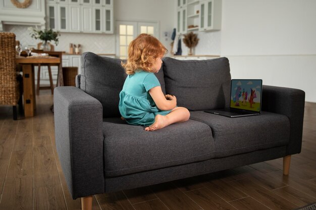 Voller Schuss Kind sitzt auf der Couch mit Laptop