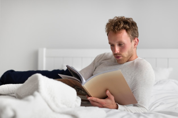 Kostenloses Foto voller schuss mann liest buch im schlafzimmer