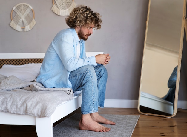 Kostenloses Foto voller schuss mann sitzt auf dem bett