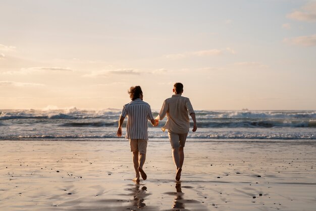 Voller Schuss schwule Männer, die am Strand Händchen halten