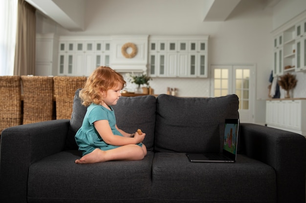 Voller Schuss süßes Kind sitzt auf der Couch mit Laptop