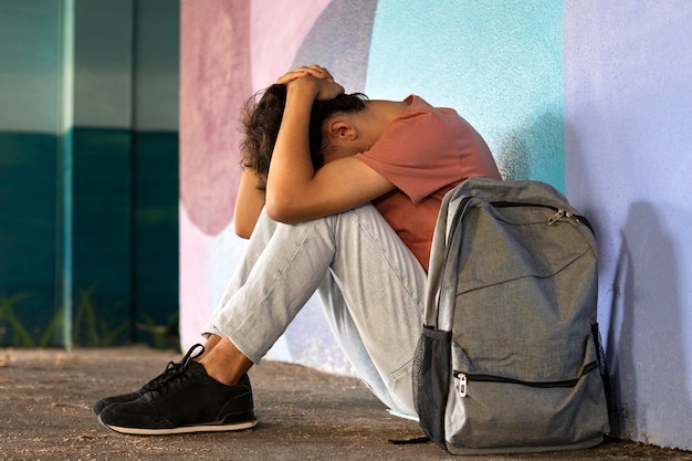 Voller Schuss trauriger Junge, der auf dem Boden sitzt