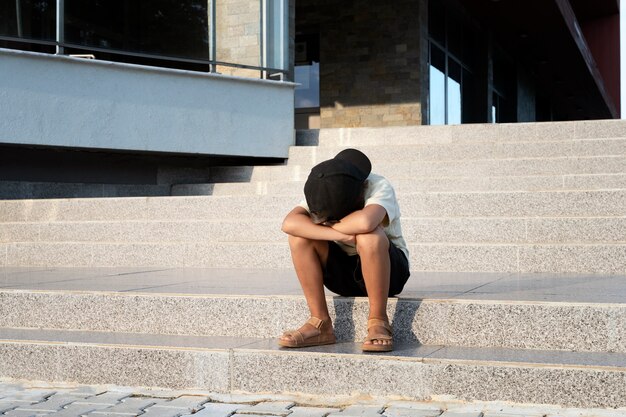 Voller Schuss trauriger Junge, der auf der Treppe sitzt