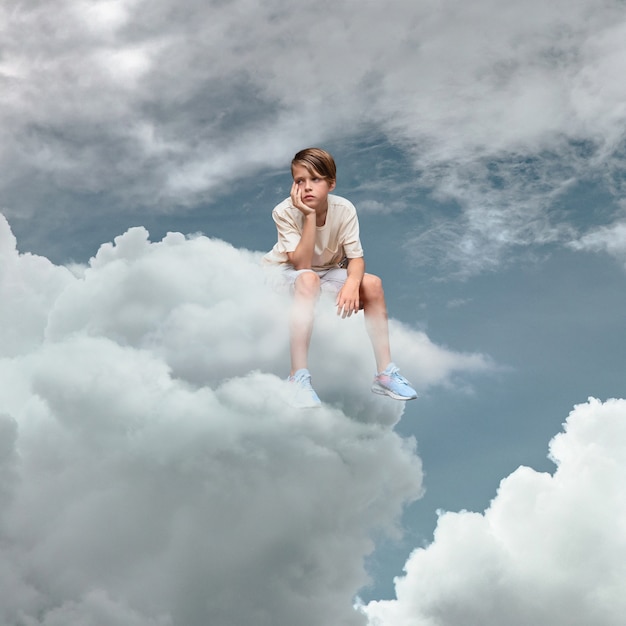 Voller Schuss trauriges Kind, das auf einer Wolke sitzt