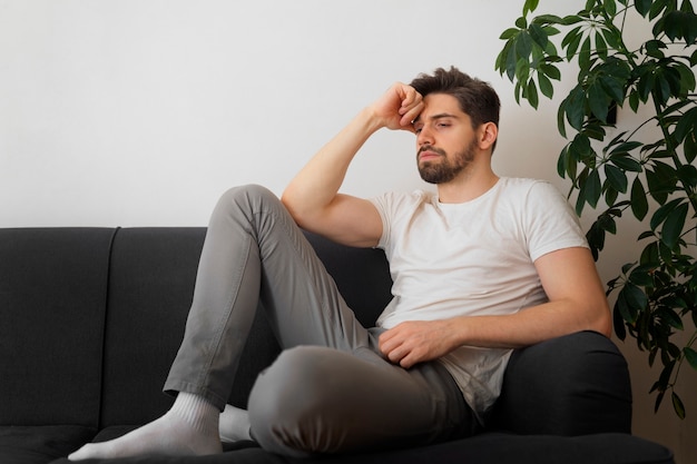 Kostenloses Foto voller schuss unsicherer mann, der auf der couch sitzt