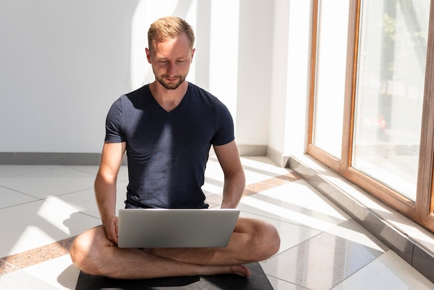 Voller Schussmann, der auf Yogamatte sitzt und Laptop verwendet