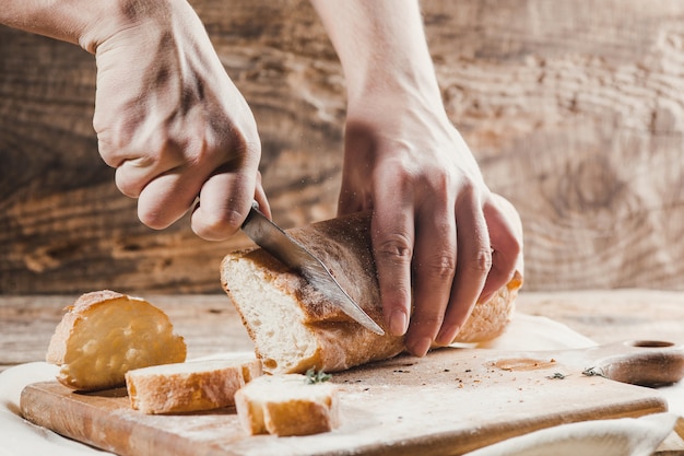 Vollkornbrot auf Küchenholzplatte mit einem Koch, der Goldmesser zum Schneiden hält.