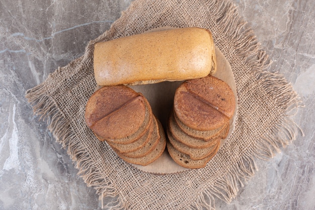 Vollkornbrot hinter Stapeln von geschnittenem Schwarzbrot auf einem Brett auf Marmor.