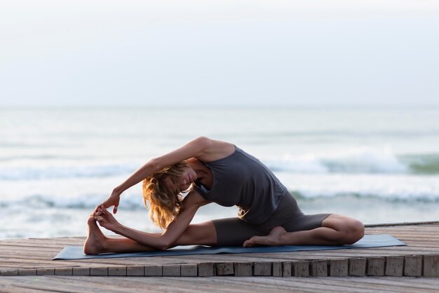 Vollschuss Frau, die Yoga auf Matte nahe Meer praktiziert