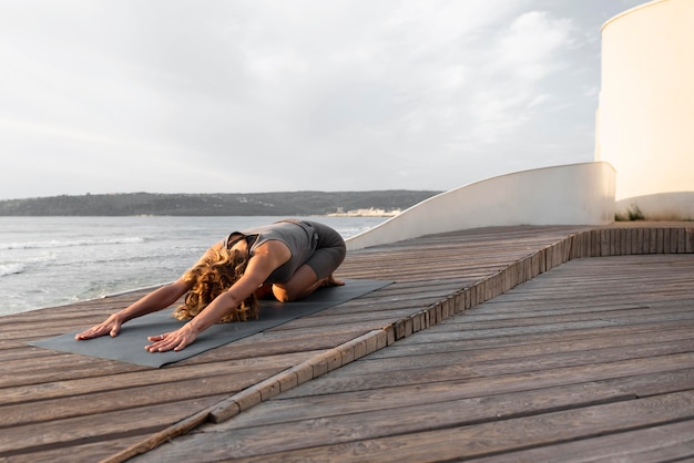 Vollschuss Frau, die Yoga-Pose draußen auf Matte praktiziert