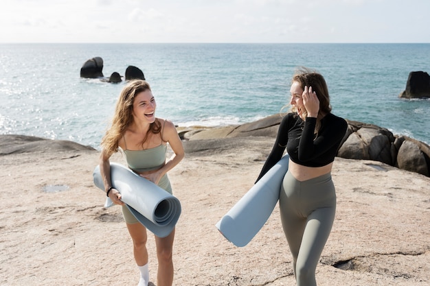 Vollschussfrauen mit Yogamatten am Strand