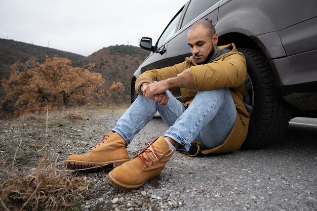 Kostenloses Foto vollschussmann, der in der nähe des autos sitzt