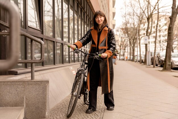 Vollständige ansicht einer lächelnden frau mit fahrrad, die auf der straße in die kamera blickt