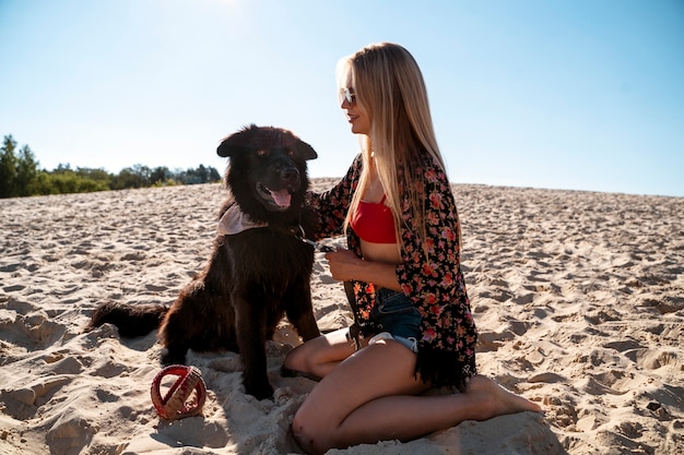 Vollständige Smiley-Frau mit Hund am Strand