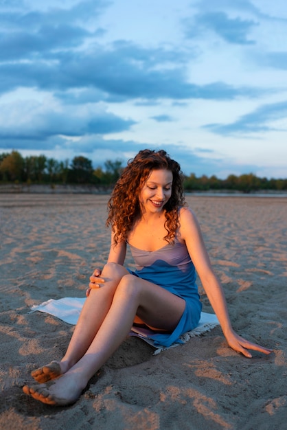 Kostenloses Foto vollständiges smiley-mädchen, das am strand sitzt