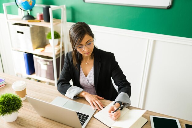 Von zu Hause aus arbeiten. Formale junge Lehrerin, die auf einem Notizbuch schreibt und ihren nächsten Unterricht zu Hause plant