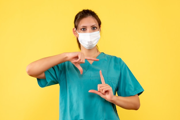 Vorderansicht-ärztin im medizinischen hemd und in der maske auf gelbem hintergrund