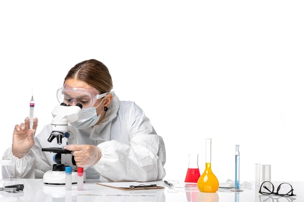Vorderansicht Ärztin im Schutzanzug und mit Maske unter Verwendung des Mikroskops auf weißem Hintergrund Covid Virus Pandemie Gesundheit Coronavirus