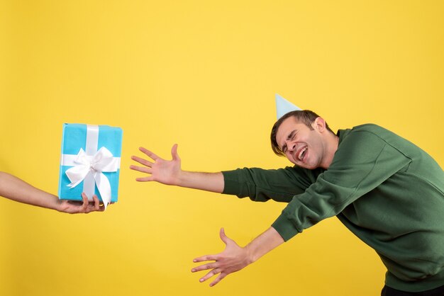 Vorderansicht aufgeregter junger Mann, der versucht, das Geschenk in der menschlichen Hand auf Gelb zu fangen
