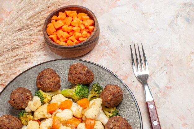 Vorderansicht Brokkoli- und Blumenkohlsalat und Fleischbällchen auf Tellerschüssel mit schneidender Karotte eine Gabel auf nacktem Hintergrund mit Kopienraum