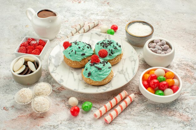 Vorderansicht bunte Bonbons mit Sahnetorten auf weißem Hintergrund Keks süße Kuchenplätzchen