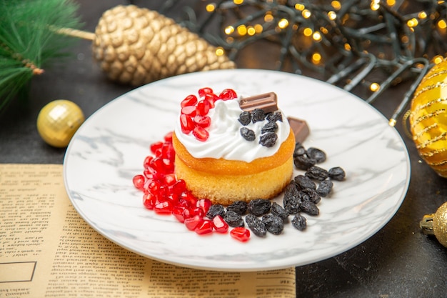 Vorderansicht cremiger Kuchen mit Rosinen und Früchten um Neujahrsbaumspielzeug auf dunklem Hintergrund Kuchen süße Fotocreme Dessert