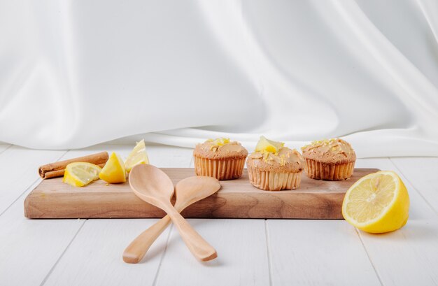 Vorderansicht Cupcakes mit Zitrone und Zimt auf einem Brett mit Holzlöffeln auf einer weißen Oberfläche