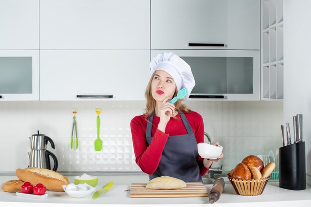 Vorderansicht denkende blonde Frau in Kochmütze und Schürze Butterbrot in der Küche