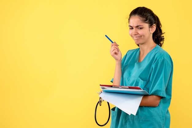 Vorderansicht denkende junge Ärztin, die Papiere prüft, die auf gelbem Hintergrund stehen