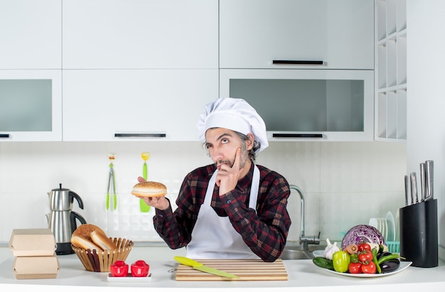 Vorderansicht denkender männlicher Koch, der Brot in der Küche hält