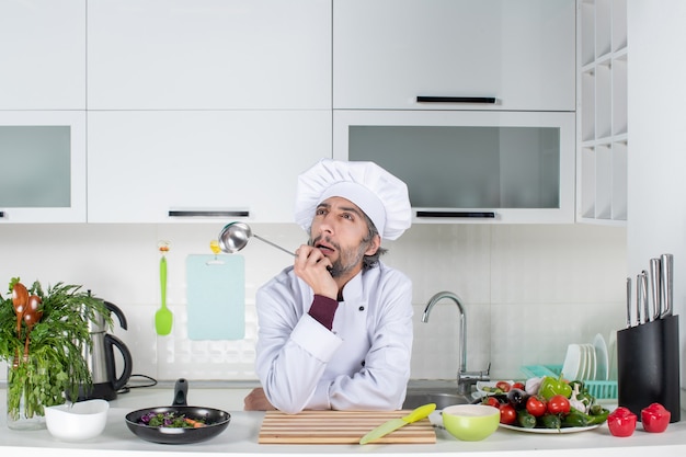 Vorderansicht denkender männlicher koch in uniform beim kochen in der küche