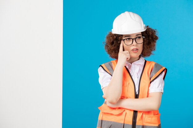 Vorderansicht denkender weiblicher Baumeister in Uniform auf blauer Wand