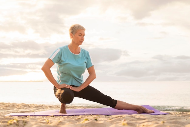 Vorderansicht der älteren Frau, die Yoga am Strand praktiziert