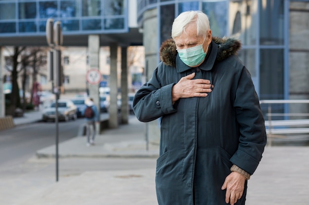 Vorderansicht der älteren Frau mit der medizinischen Maske, die sich krank fühlt, während in der Stadt