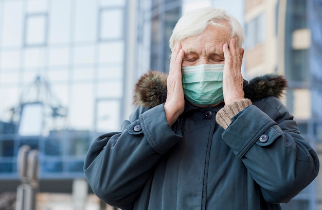 Kostenloses Foto vorderansicht der älteren frau mit der medizinischen maske, die sich nicht gut fühlt, während sie draußen ist