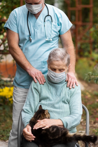 Vorderansicht der älteren Frau mit der medizinischen Maske und der Katze, die von einer männlichen Krankenschwester gepflegt werden