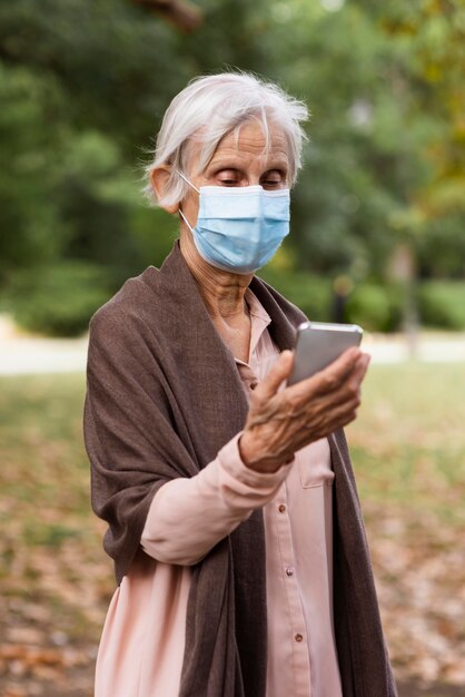 Vorderansicht der älteren Frau mit medizinischer Maske und Smartphone