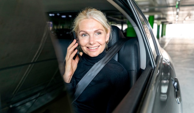 Vorderansicht der älteren Geschäftsfrau des Smileys, die das Telefon im Auto spricht