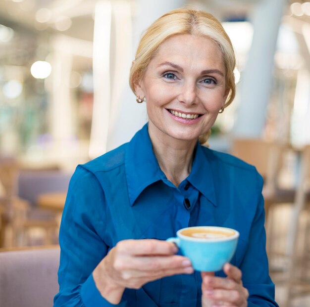 Vorderansicht der älteren Geschäftsfrau des Smileys, die Tasse Kaffee während der Arbeit genießt