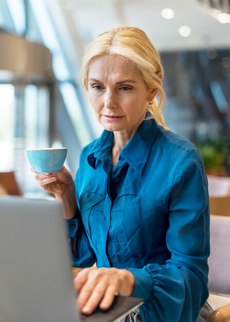 Vorderansicht der älteren Geschäftsfrau, die am Laptop arbeitet und Tasse Kaffee hält