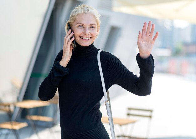 Vorderansicht der älteren Smileyfrau im Freien auf einem Telefonanruf und Winken