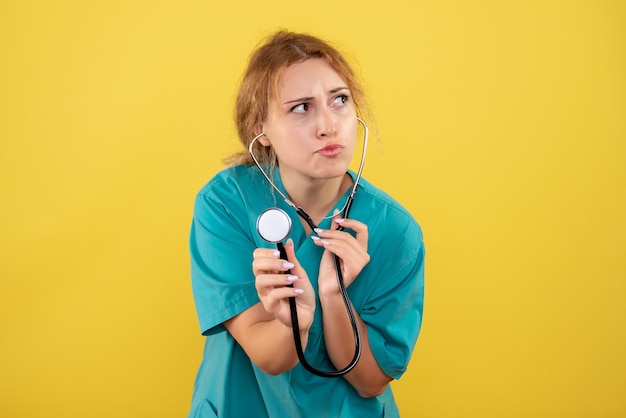 Kostenloses Foto vorderansicht der ärztin im medizinischen hemd mit stethoskop auf gelber wand